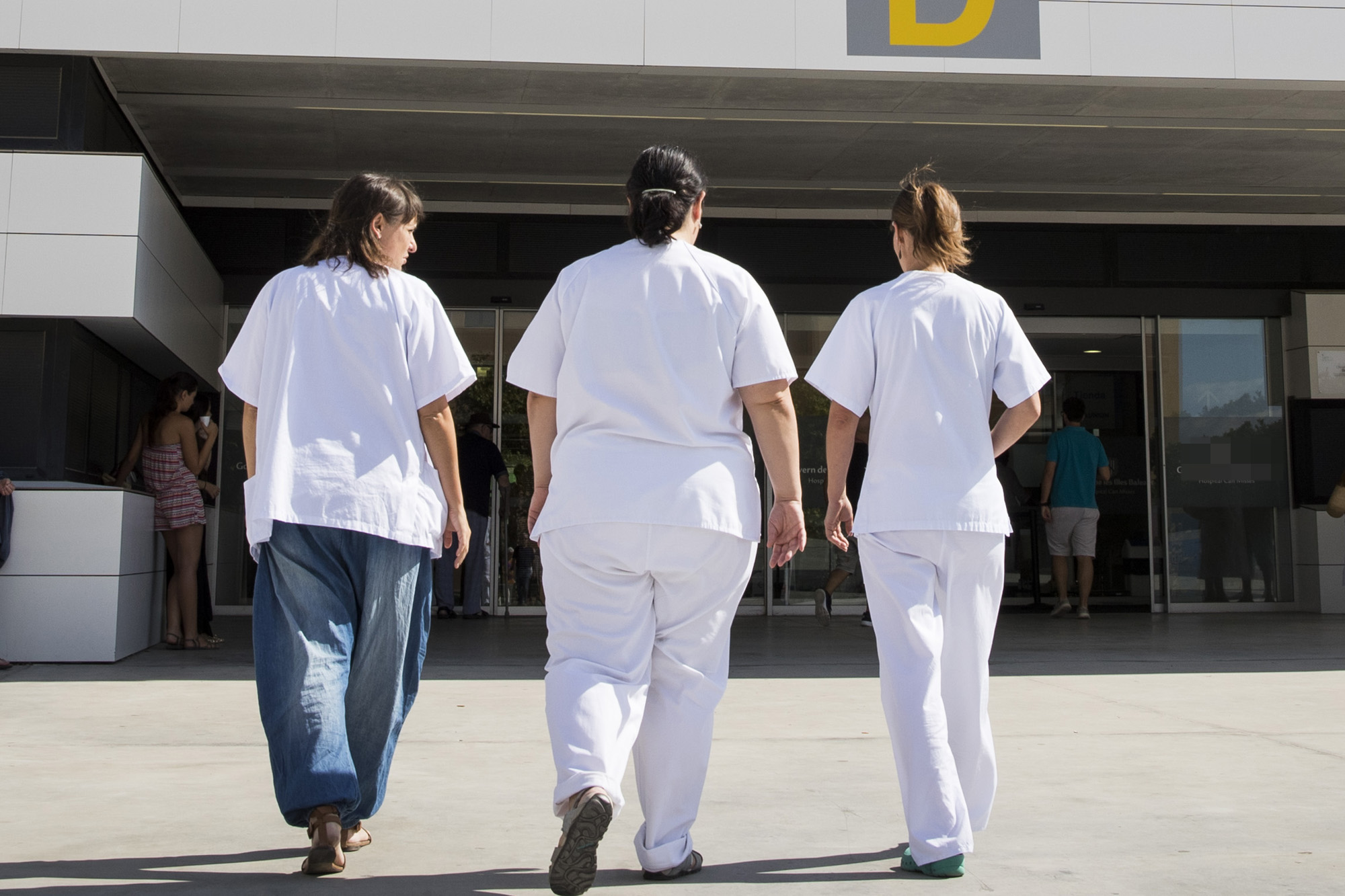 Three workers from the Hospital "Can Misses" enter the building on the island of Ibiza, on August 11, 2017. Known as much as a wild party island as a place of tranquility with coves of turquoise blue water, Ibiza has increased in popularity over the years. But behind the sea, sun, dancing and yachts lurks a serious problem of tourism overcrowding that is preventing many locals from finding affordable accommodation. / AFP PHOTO / JAIME REINA